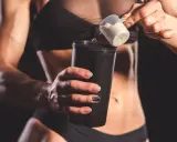 Kobieta z umięśnionym brzuchem dodaje proszek do shakera. Czy shake proteinowy jest zdrowy? To zależy od składu.