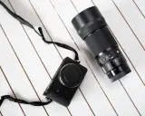 Makrofotografia sprzęt: czarny aparat Sigma fp z obiektywem 105mm f/2.8 DG DN Macro Art na białym, drewnianym tle.