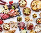 Una mesa llena de aperitivos baratos para mucha gente: embutidos, quesos, aceitunas, frutos secos, pimientos, pepinillos y pan.