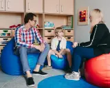 Ojciec, syn i terapeuta dla dziecka rozmawiają w przytulnym pokoju. Na ścianie wisi tablica sensoryczna.