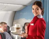 Uśmiechnięta stewardessa w czerwonym mundurku podaje kawę. Czy jej stewardessa zarobki są wysokie?