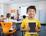 Un bambino sorridente in classe mostra un tablet, pronto per le attività di accoglienza di un nuovo alunno.