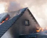 Un incendie maison ravage le toit, des flammes vives et une épaisse fumée s'échappent des tuiles.