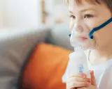 Chłopiec z maską inhalacyjną na twarzy, korzystający z nebulizatora. Pomaga mu to w leczeniu kataru.