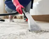 Osoba w różowych rękawiczkach używa odkurzacza piorącego, pokazując, jak wyczyścić dywan.
