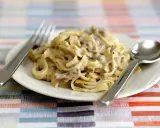 Un piatto di tagliatelle ai funghi cremose, pronte per essere gustate con forchetta e cucchiaio.