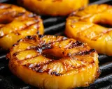 Saftige Ananasscheiben mit Grillstreifen auf einem Rost. Das Ananas grillen verzaubert mit süß-karamelliger Note.