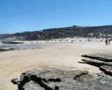 Sonniger Strand bei Monte Clerigo mit Felsen und Menschen, die sich im Wasser und am Ufer aufhalten.