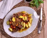 Plato de rabo de toro estofado con patatas y zanahorias, bañado en una salsa de vino blanco.