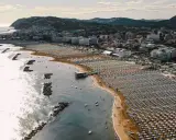Vista aerea della cattolica spiaggia, con file ordinate di ombrelloni e lettini che si estendono lungo la costa, mentre il mare luccica sotto il sole.