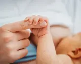 Dłoń noworodka ściska palec dorosłego. Delikatny uścisk, który budzi pytanie: czy można przekarmić noworodka?