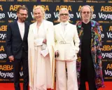 Członkowie zespołu ABBA na czerwonym dywanie, pozujący do zdjęć przed banerem "ABBA Voyage".
