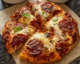 Gotowe ciasto na pizzę z pepperoni, ciągnącym serem i listkami bazylii, pachnące i apetyczne.
