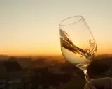 Ein Glas Scheurebe Wein schwenkt im warmen Abendlicht vor einer malerischen Landschaft.