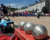 Boules de jeu en gros plan, prêtes pour une partie de boule lyonnaise. Des joueurs s'affrontent en arrière-plan.