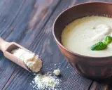 Sauce crémeuse à la sauce parmesan italienne, garnie de basilic frais. Une cuillère en bois contient du parmesan râpé.