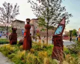 Sculture arrugginite e vegetazione rigogliosa nel Parco Fellini a Rimini, con il castello Sismondo sullo sfondo.