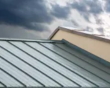 Dunkle Wolken über einem modernen Metalldach. Die glänzenden Aluminiumbahnen reflektieren das Licht, doch die Nachteile wie Geräuschentwicklung bei Regen sind nicht sichtbar.