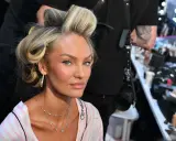 Blond włosy modelki w lokach, delikatny air touch. W tle wizażystka i kosmetyki.