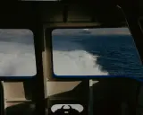 Vue depuis la cabine d'un bateau, avec le sillage blanc de l'eau. Au loin, une ville côtière et des grues de port. Les canaux VHF marine sont essentiels pour la communication.