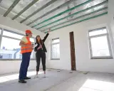 Inspektor budowlany i kobieta omawiają projekt. Widoczny sufit podwieszany jednopoziomowy z drewnianymi belkami i izolacją.