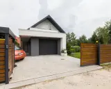 Nowoczesny podjazd z kostki brukowej, co zamiast kostki na podjazd? Elegancki dom z garażem, drewniane ogrodzenie i pomarańczowy samochód.