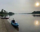 Två kajaker vid en sandstrand, redo för en paddling. Solen lyser svagt genom diset. Frågan är hur långt paddlar man på en dag?