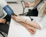 Lekarz mierzy ciśnienie krwi pacjentowi. Na ramieniu pacjenta założony jest mankiet ciśnieniomierza, a lekarz słucha przez stetoskop.