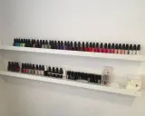 Dwie białe półki wypełnione po brzegi kolorowymi buteleczkami. To idealna półka na lakiery dla każdej miłośniczki manicure.