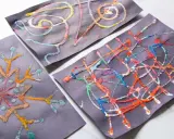 Kinder malen auf schwarzem Papier mit bunten Salzkristallen. Ein Bild zeigt eine Schneeflocke, die anderen abstrakte Muster.