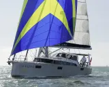 Le voilier "Noranna" L430 navigue sur une mer agitée, sa grand-voile aux couleurs vives bleu et jaune captant le vent.