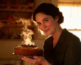 Une femme souriante présente un gâteau moelleux chataigne fumant, décoré de marrons.