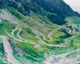 Kręta droga Transalpina wijąca się po zielonych zboczach gór. Widok z lotu ptaka na serpentyny i mosty.