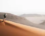 Läufer erklimmt eine Sanddüne, bereit für den Marathon des Sables. Die Wüstenlandschaft erstreckt sich in der Ferne.