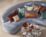 Sofá curvo gris con cojines de terciopelo y estampados geométricos. Un diseño moderno y acogedor.