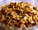 Pyszna sałatka z makaronem farfalle, kurczakiem, kukurydzą i suszonymi pomidorami, posypana natką pietruszki.