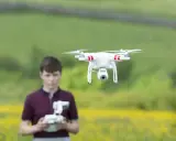Ein Junge steuert eine Drohne in Litauen. Die Drohne schwebt über einem Feld mit gelben Blumen.