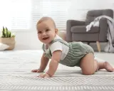 Uśmiechnięte 8 miesięczne dziecko na czworakach na dywanie.