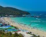 Ein belebter Pattaya Strand mit vielen Menschen, Sonnenschirmen und Booten im türkisfarbenen Meer.