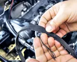 Uszkodzony pasek osprzętu, który wymaga wymiany, widać na dłoniach mechanika.