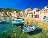 Barchette azzurre in un mare cristallino, un invito a scoprire dove andare al mare in Croazia. Case di pietra e colline verdi fanno da sfondo.