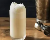Ein cremiger Ramos Gin Fizz mit üppigem Schaum. Daneben ein Jigger und ein Shaker, bereit für den nächsten Drink.