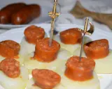 Chorizo a la sidra en rodajas, servido sobre patatas y adornado con espadas doradas.