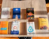 Una collezione di **libri** di Gianluca Gotto disposti su un tavolo di legno. Tra i titoli: "Le coordinate della felicità", "Come una notte a Bali", "La Pura Vida".
