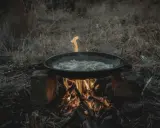 Cuisine en plein air sur un réchaud rocket stove improvisé. Une poêle cuit des aliments sur un feu vif.