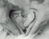 Manos de padre formando un corazón alrededor de los pies de su bebé, un símbolo de apego excesivo al padre y amor incondicional.