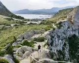 Ein Wanderweg schlängelt sich durch das steile **Gebirge Mallorcas** mit Blick auf eine Bucht.