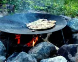 Matlagning över öppen eld på ett muurikka ställning. Pannkakor steks i en stor stekpanna över glödande kol och ved.