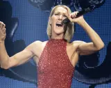 Celine Dion idag, i en glittrig röd klänning, sjunger passionerat med mikrofonen i handen och armarna utsträckta.