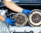 Mechanik w niebieskich rękawiczkach trzyma części samochodowe. Wygląda na to, że właśnie wymienia ślizgające się sprzęgło.